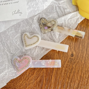 Three acetate heart hair clips with marble patterns and rhinestones on wood background