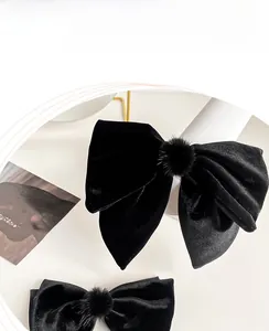Detail of elegant black velvet bow hair clip with central fuzzy pom pom texture