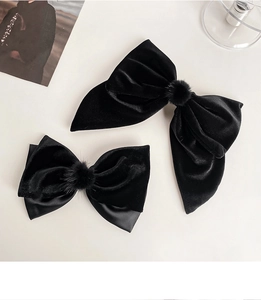 Macro detail of black velvet bow hair clips with plush faux fur ball accents