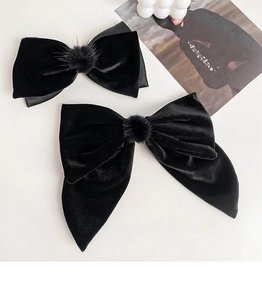 Detail of black velvet bow hair clips with soft fur pom-poms on white background
