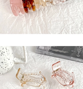 Detail of colorful resin hair claw clips with metal springs on a textured white background