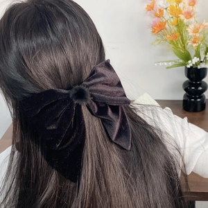 Elegant large black velvet bow hair clip with pom-pom detail on model's hair