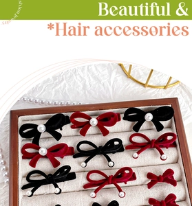 Detail of red and black velvet bow hair clips with pearls displayed on a wooden tray