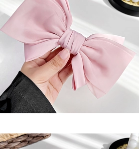 Close-up of a large pink satin bow hair clip held in hand showing soft texture and size