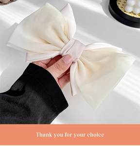 Detail of a creamy satin bow hair clip held by hand under soft natural window shadows