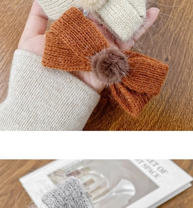 Detail view of knitted bow hair clips with soft pom-poms in cream, orange and grey colors