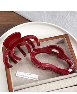 Detailed view of two deep red shark hair claws in spider and wavy shapes in a wooden tray