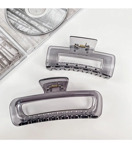 Close-up of two transparent grey resin rectangular hair claws with metal springs