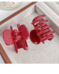 Detail of two large glossy red hair claws on a beige velvet tray for elegant hairstyling
