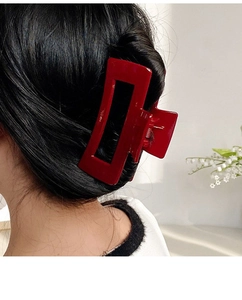Detail of a large red rectangular hair claw clip shown on a woman from a side-back view