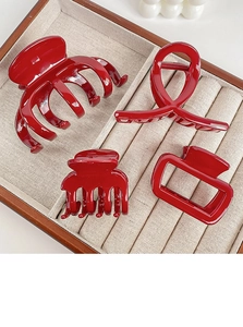 Detail view of four glossy red hair claw clips in varied styles on a linen tray