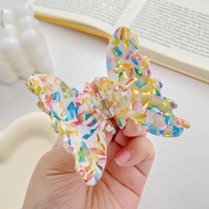 Pince à cheveux papillon colorée en acétate tenue à la main avec décor esthétique