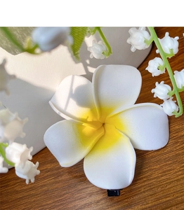Detailed macro view of a creamy white plumeria flower hair claw with yellow center