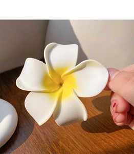 Macro shot of a yellow and white EVA frangipani flower hair clip held by hand