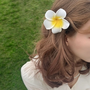 Tropical frangipani flower hair claw clip with white petals and yellow center on wavy hair