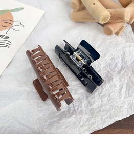 Close-up of square acrylic hair claws in black and caramel brown on minimalist background