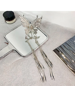 Détail d'une pince à cheveux papillon évidée argentée avec de longs glands métalliques