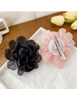 Détail d'une pince à cheveux rose en tissu montrant le clip en métal et les pétales drapés