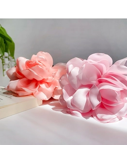 Close-up of elegant coral and pink fabric flower hair clips on a minimalist white surface