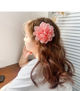Gros plan sur une pince à cheveux fleur rose en tissu portée par un mannequin au soleil
