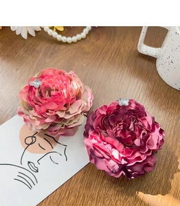 Detail view of pink and rose silk peony flower hair clips with butterfly accents on wood