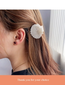 Détail d'une pince à cheveux en forme de coquillage blanc avec strass sur cheveux