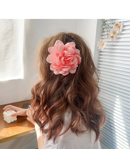 Détail d'une grande pince à cheveux fleur en tissu rose pâle sur des cheveux bruns