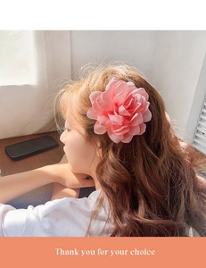 Détail d'une pince à cheveux rose poudré en forme de rose sur de longs cheveux bouclés