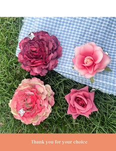 Detailed view of four assorted fabric floral hair clips on a green lawn and plaid cloth
