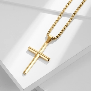 Polished gold stainless steel cross necklace displayed on a white geometric stand