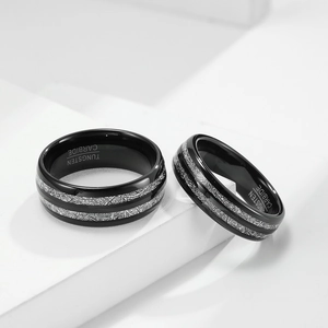 Polished black tungsten carbide ring with dual silver inlay textures on white pedestal