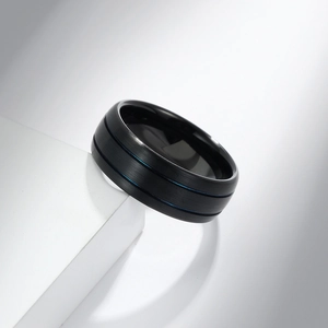 Matte black tungsten steel ring with dual blue grooves on white geometric stand