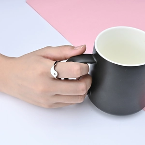 Close-up of Tai Chi Yin Yang ring on hand holding a matte black mug with pink background