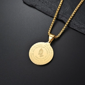 Détail macro du pendentif mains en prière doré avec gravure de la prière de sérénité