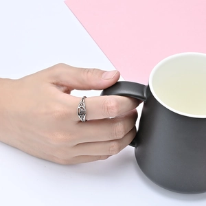Polished silver stainless steel ring with Celtic knot design worn on hand with mug