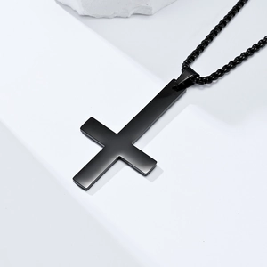 Close-up of matte black inverted cross pendant with matching beaded chain on white steps