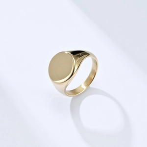 Close-up of a gold-plated signet ring with a polished round flat top and minimalist design