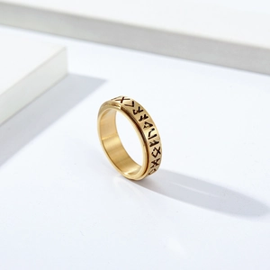 Golden stainless steel Viking spinner ring with engraved runes on a white pedestal