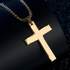 Detailed view of polished golden stainless steel cross pendant on a black textured stand