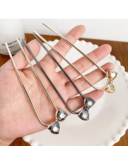 Detailed macro view of U-shaped hairpins with rhinestone bow accents in gold and gunmetal