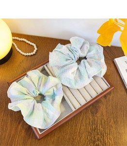 Macro shot of two pastel ruffled fabric scrunchies displayed on a wooden jewelry tray