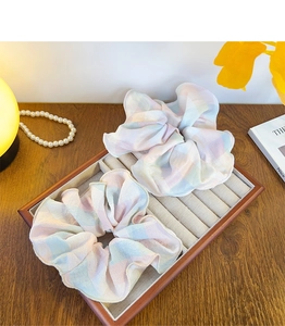 Detail view of two large plaid chiffon hair scrunchies on a soft beige velvet tray