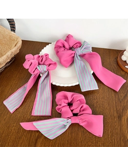 Détail de trois chouchous en mousseline rose avec de longs rubans sur une assiette en céramique