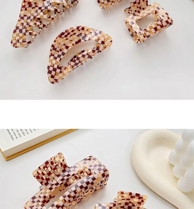 Close-up of checkered acetate hair claws in amber and beige colors on a minimalist desk