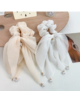 Détail de chouchous à rubans crème et blanc avec perles élégantes sur un plateau en bois