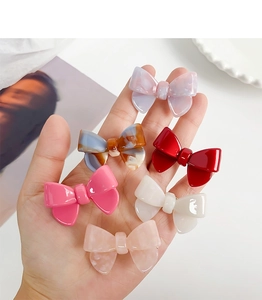 Macro detail of six colorful acetate bow hair clips held in hand against white background