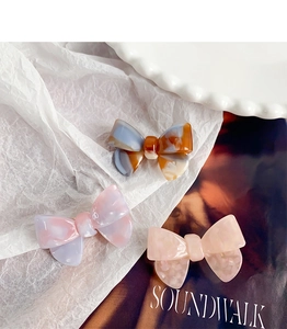 Detailed view of three acetate bow hair clips in navy, purple, and soft pink marble