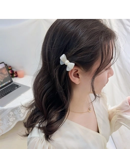 Close-up of a white acetate bow hair clip worn by a model in a natural setting