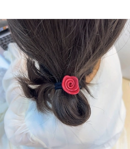 Detailansicht eines roten Acetat-Rosenhaargummis auf braunem Haar für Styling