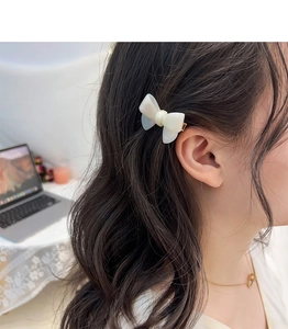 Detail view of a cream white acetate bow hair clip worn as a side accessory by a model